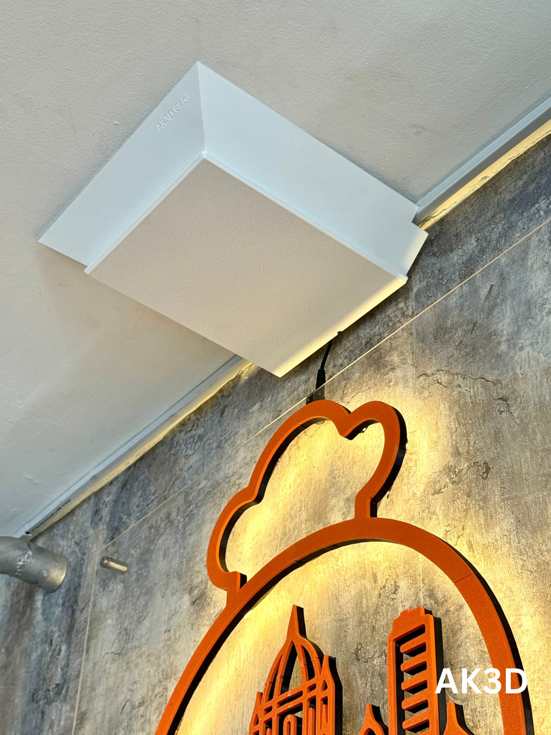 White 3D printed cover box mounted on the ceiling above the sign, with a single cable running down to the logo