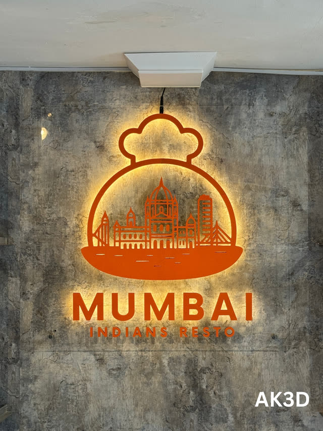 Orange Mumbai Indians Resto logo sign glowing with warm LED backlight on a concrete-look wall