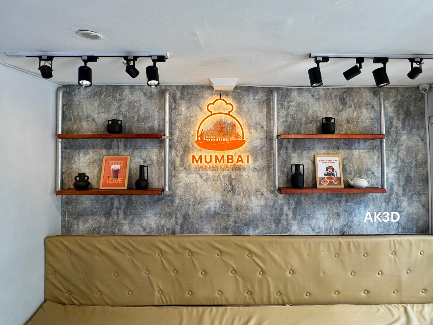The restaurant wall with the lit logo sign centered between two sets of shelves and track lights
