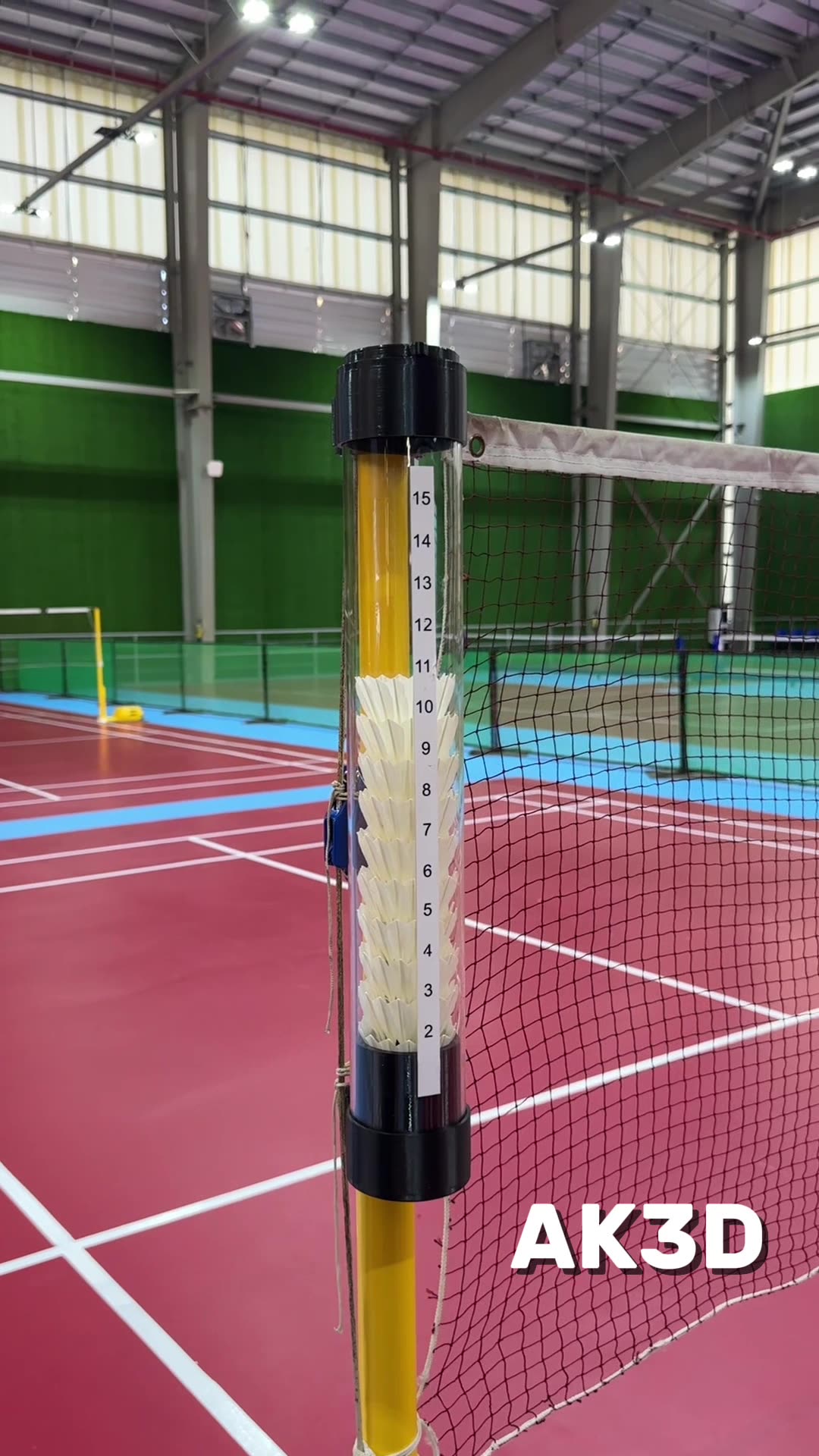 Clear tube shuttlecock holder with black 3D printed caps attached to a yellow badminton net pole